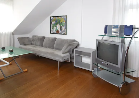 Wohnbereich unter der Dachschräge mit grauem Sofa und Blumenbild