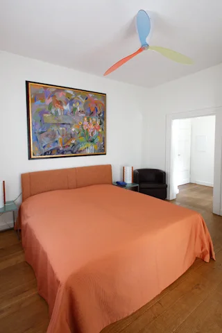 Schlafzimmer mit orangefarbener Tagesdecke und großformatigem Gemälde